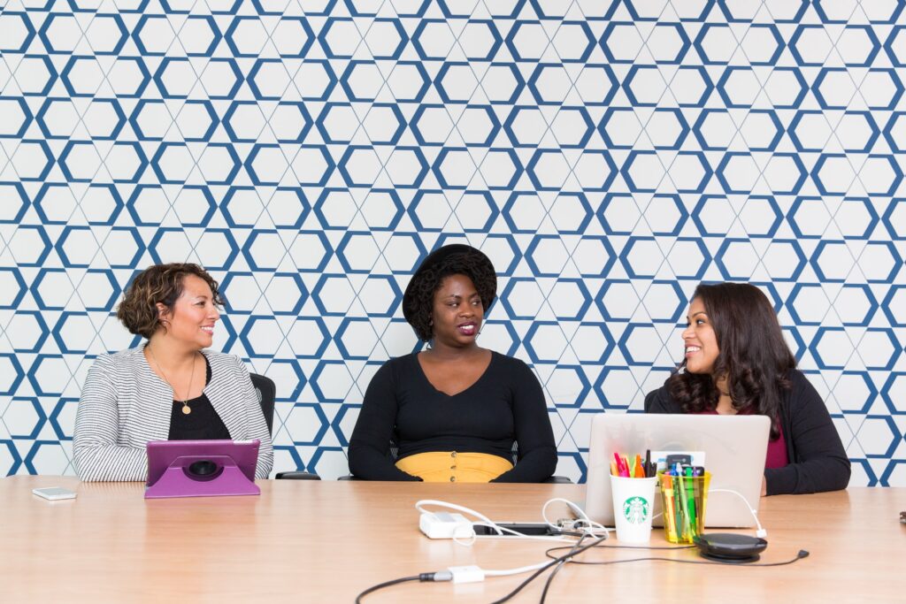 three women sitting at a work desk talking with each other. Are they happy with their work? Do they have a great job match?